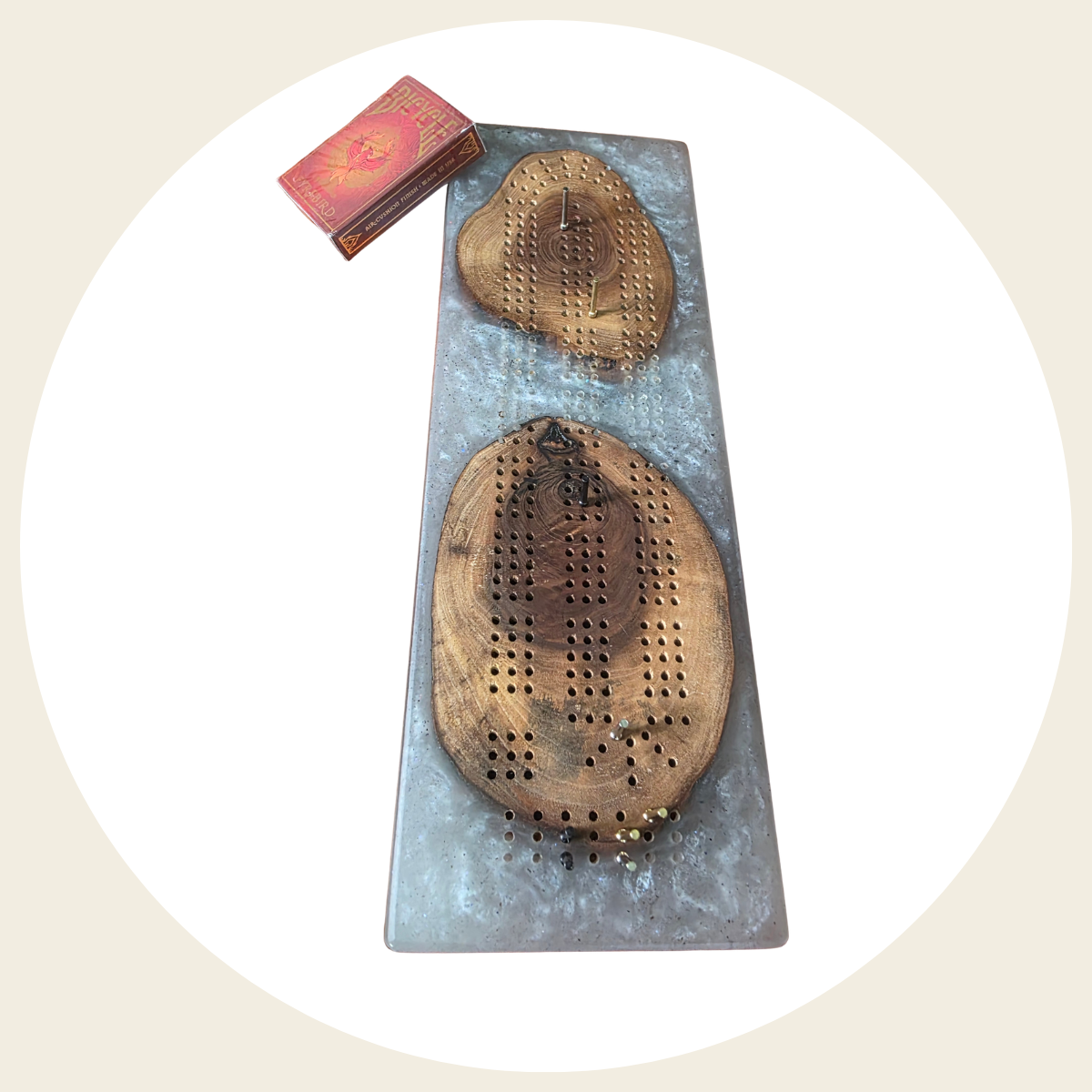 Handcrafted wood and resin cribbage board with metal pegs, displayed among green leaves