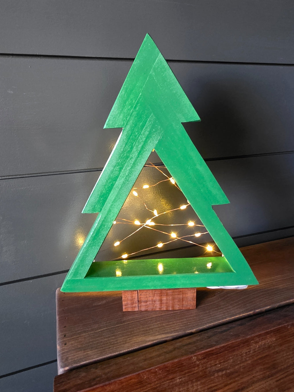Rear view of green-painted pine Christmas tree with fairy lights and walnut base