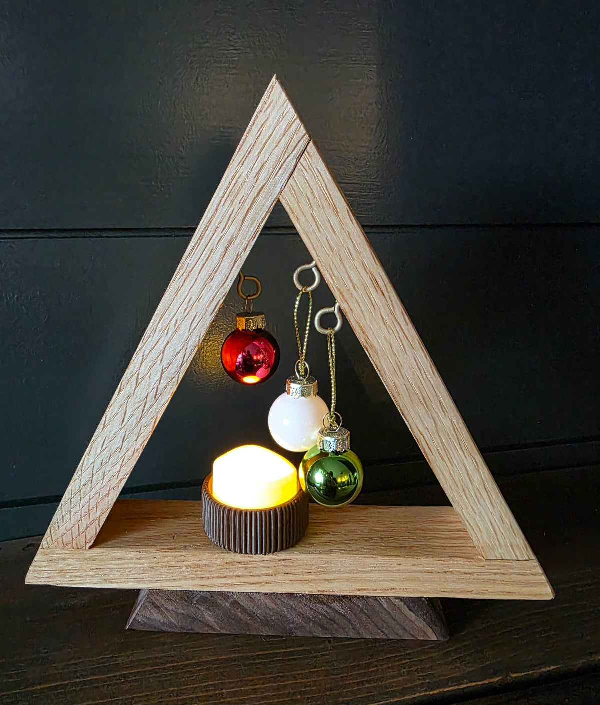 White oak triangular Christmas tree on a dark walnut base with hanging ornaments and glowing LED tea light
