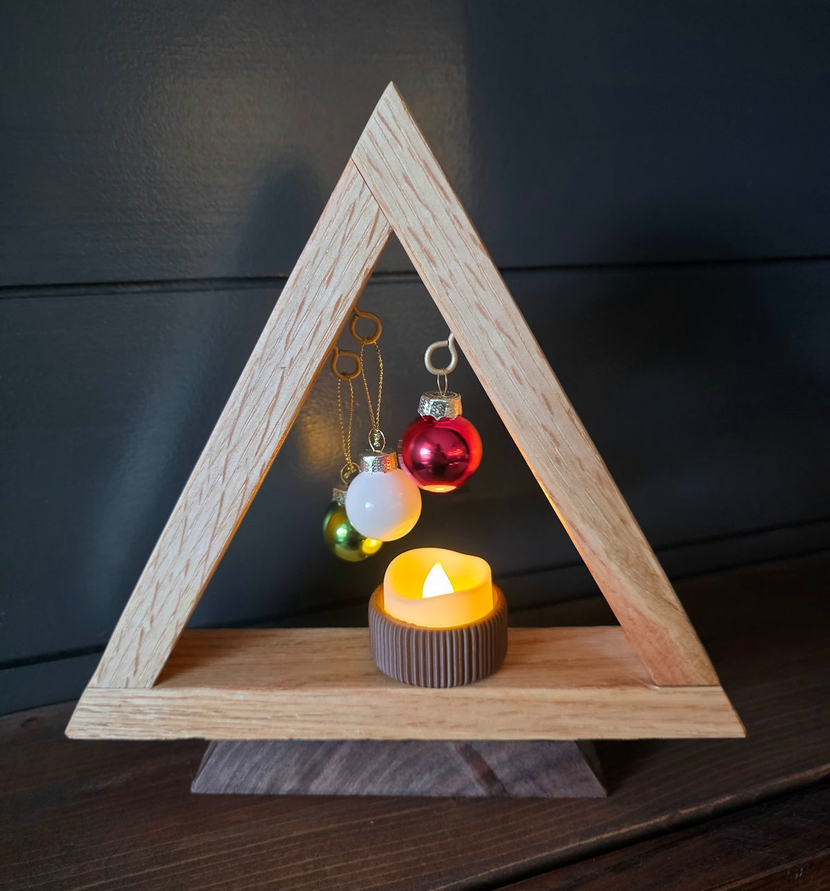 Alternate view of white oak Christmas tree with red, white and green ornaments above a flickering battery tea light