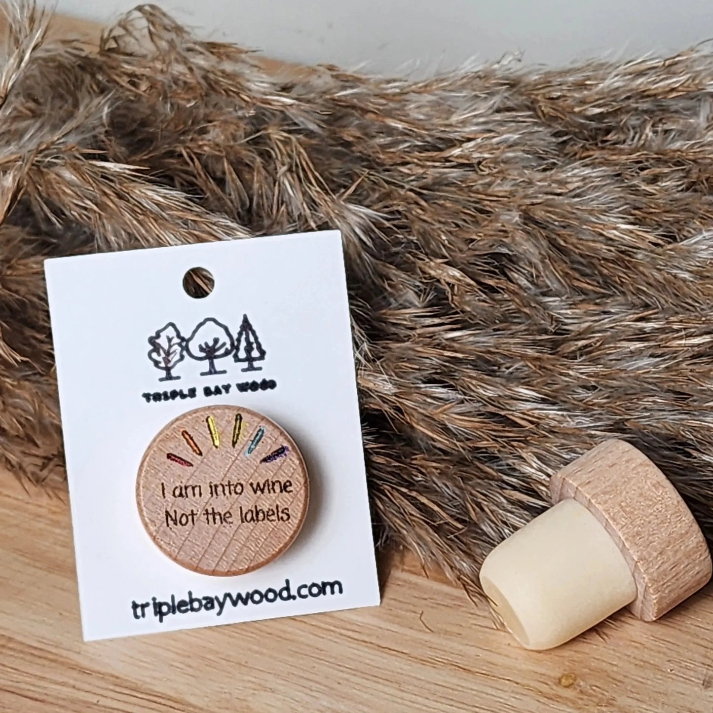 Wood wine bottle stopper with engraved text and rainbow accent, displayed on rustic background.