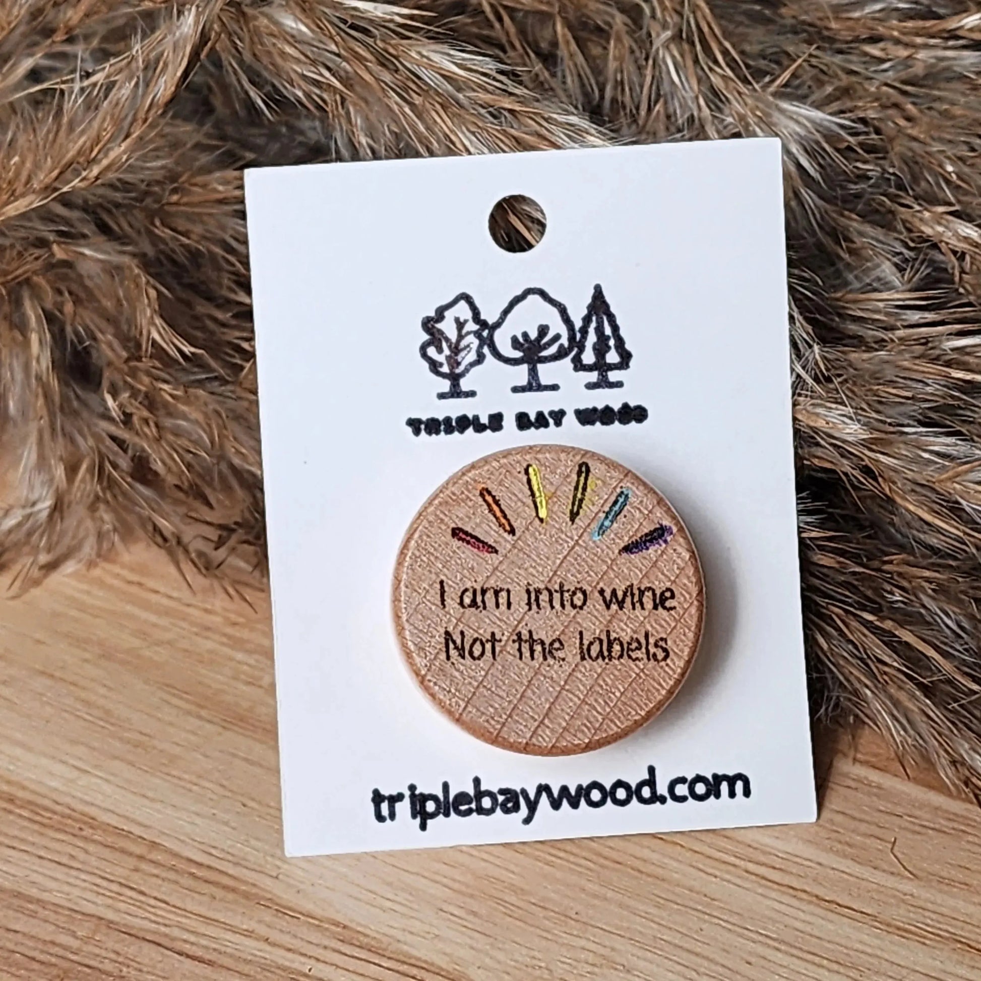 Round wooden pin with engraved 'I am into wine not the labels' text and rainbow accents on card.
