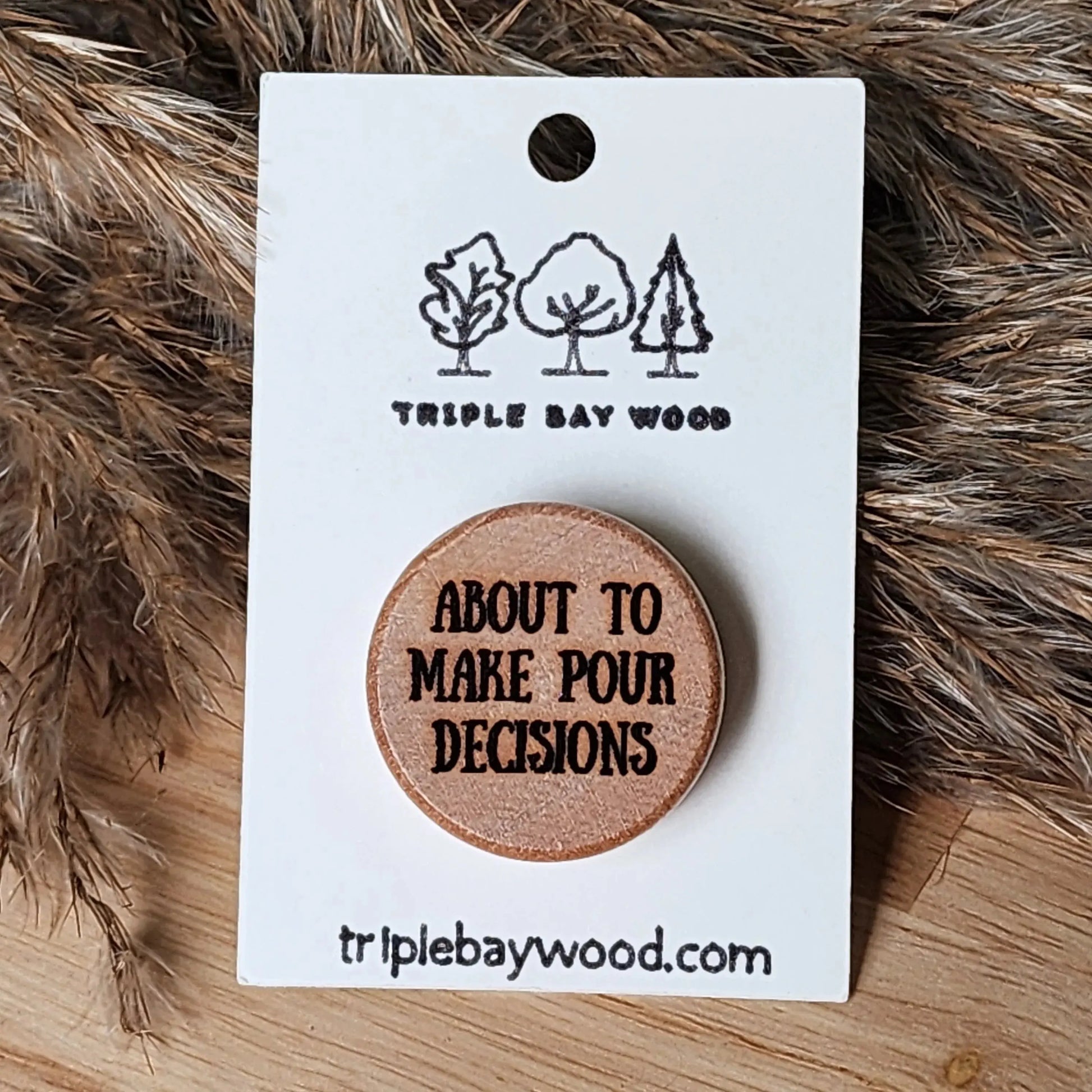 Laser-engraved wooden pin with 'about to make pour decisions' text on backing card