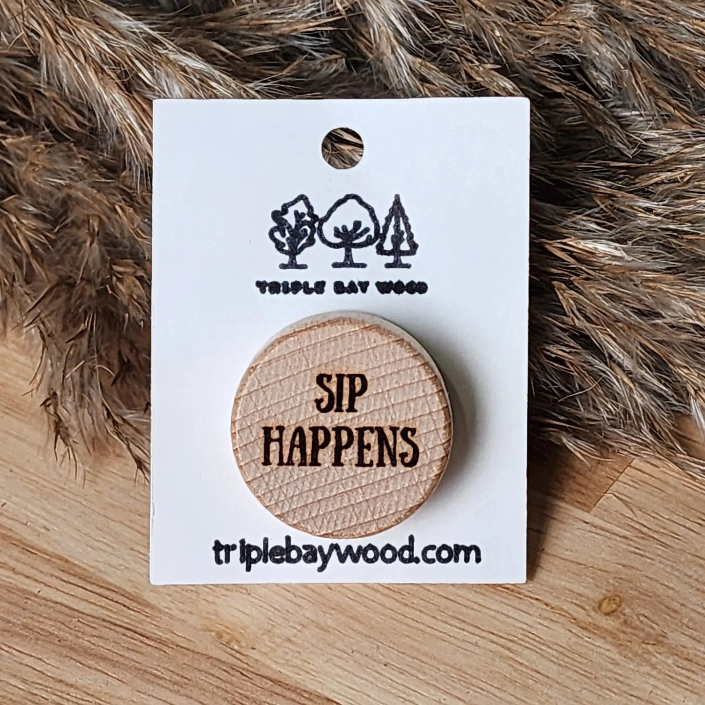 Round wood pin engraved with 'SIP HAPPENS' on display card, rustic background