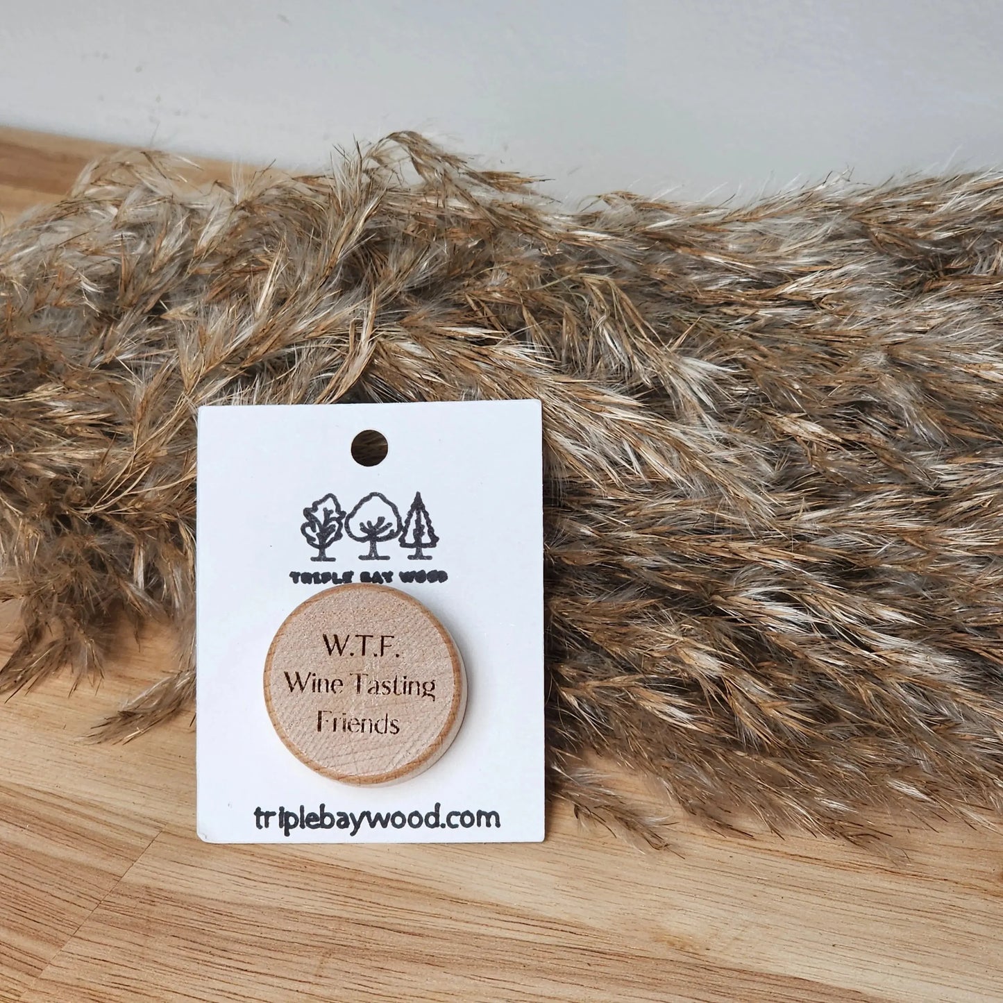 Wood wine stopper engraved with W.T.F. Wine Tasting Friends on table with dried grass