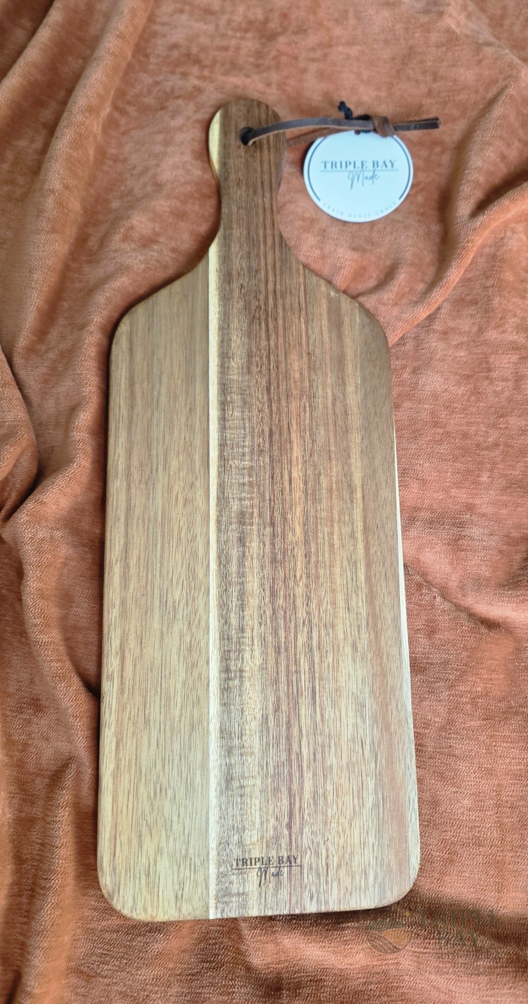 Back of acacia paddle serving board showing natural wood grain and maker mark