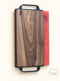Front of premium walnut serving tray with coral-red resin edge and black loop handles