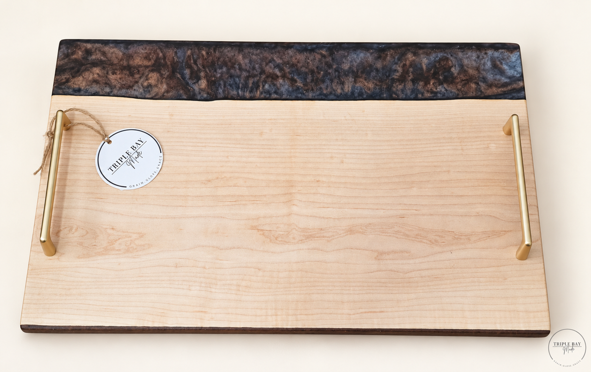 Live edge ambrosia maple serving tray with dark smoky resin edge and gold-tone handles, front view