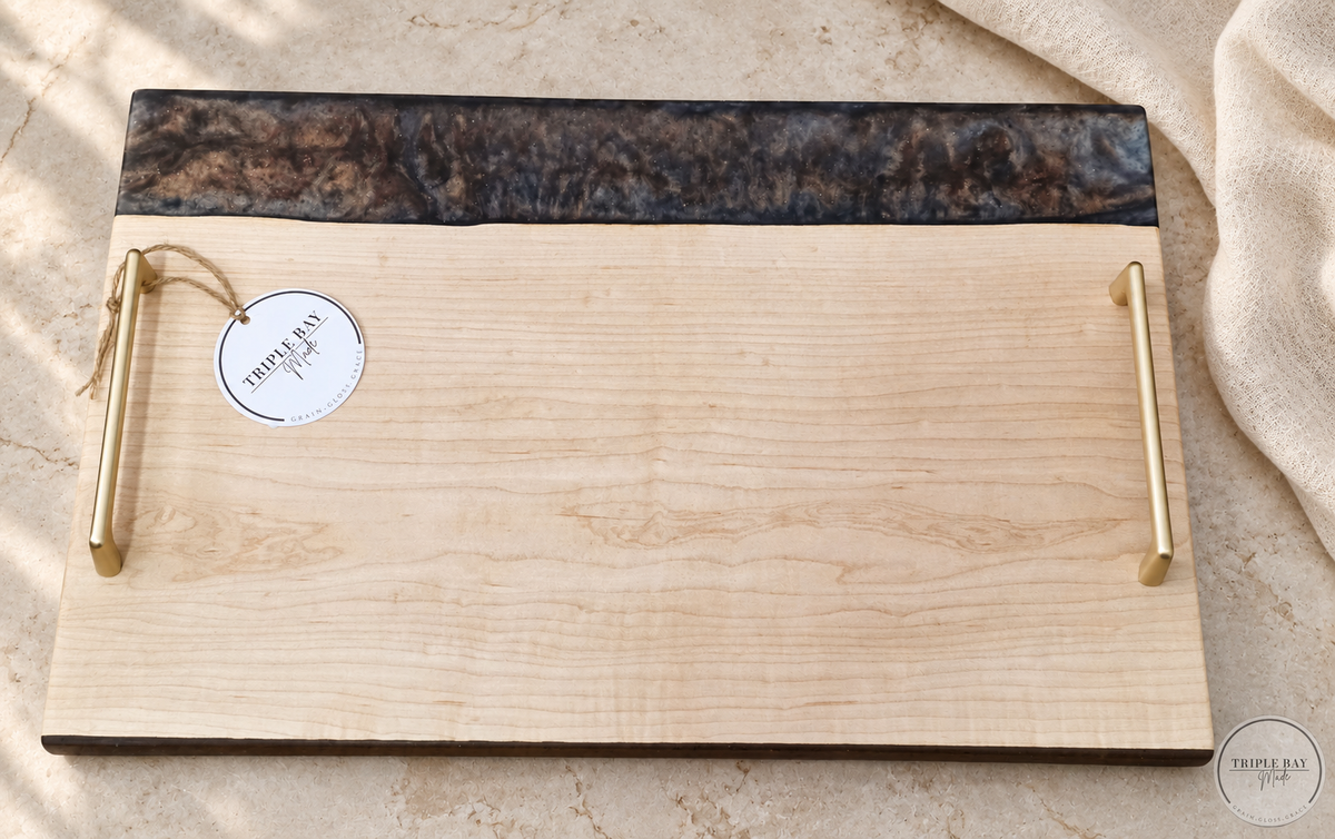 Ambrosia maple and smoky resin tray with gold-tone handles on light stone beside ivory linen