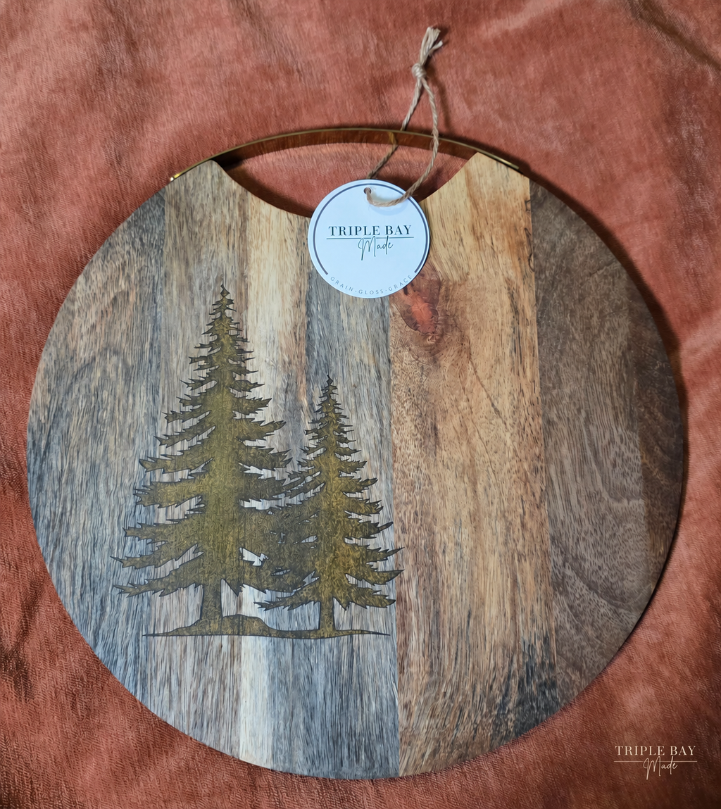 Golden Evergreens round acacia serving board with two golden resin trees and brass handle