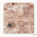 Square end-grain cutting board with bee, flower and honeycomb corner engraving on a neutral background