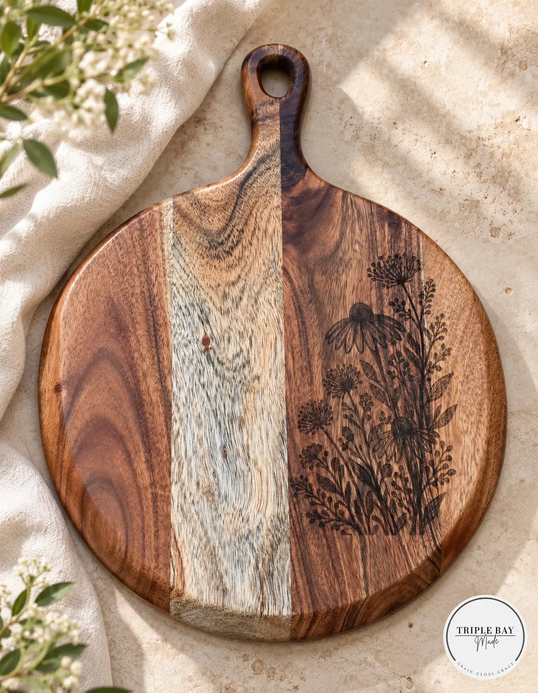 Wildflower engraved acacia paddle board on warm stone with cream linen and small flowers
