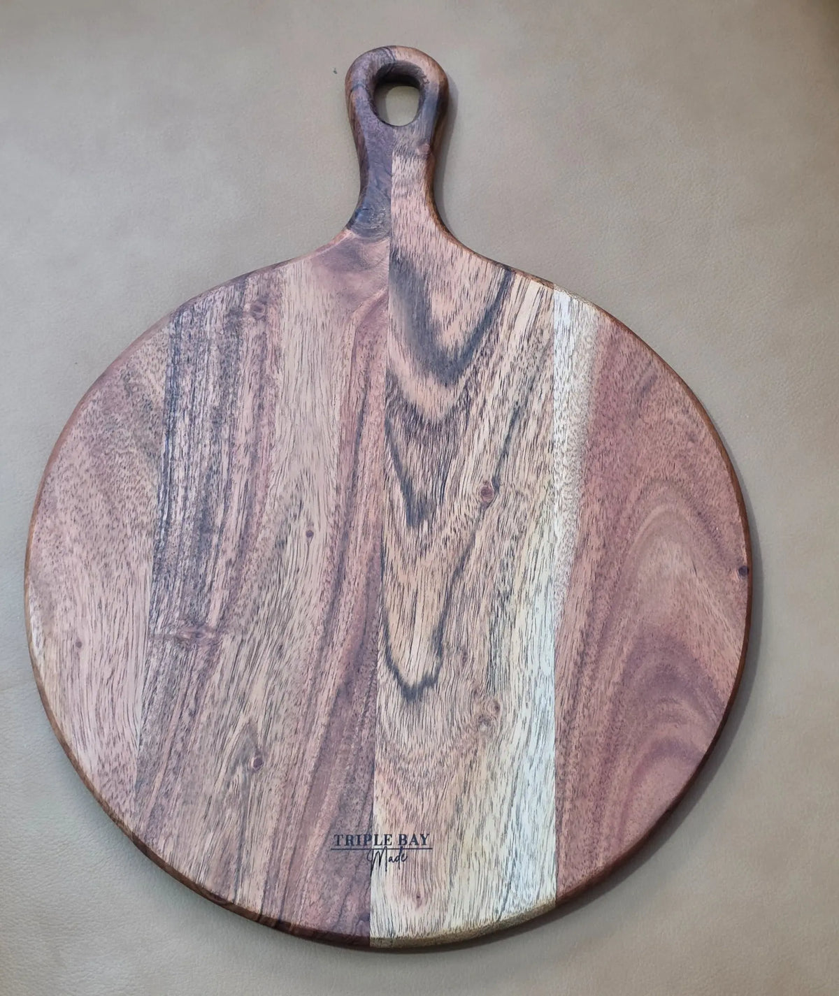 Reverse of round acacia paddle board showing contrasting pale and brown grain and Triple Bay Made maker mark