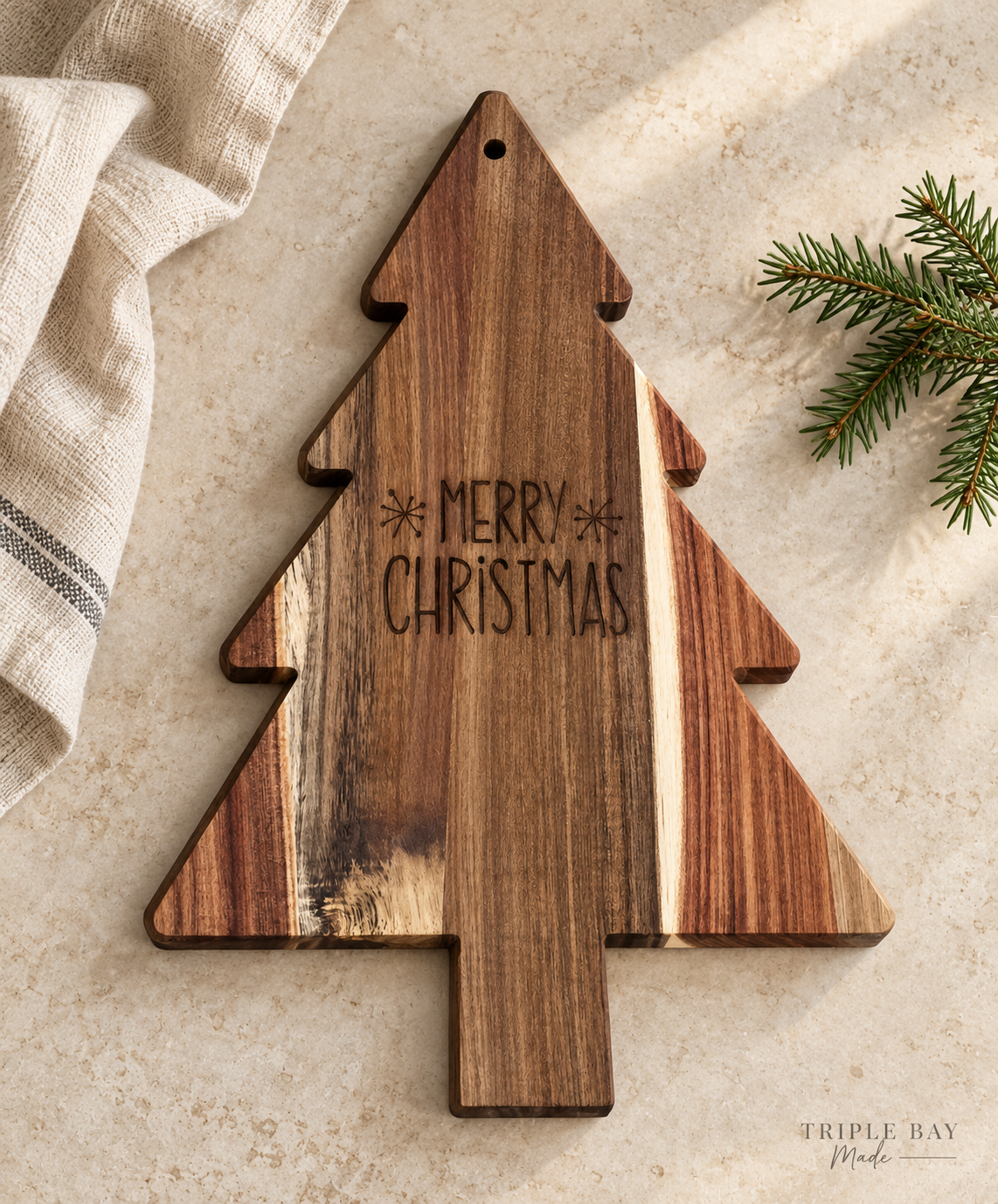 Acacia Christmas tree board styled on a warm stone counter with linen and evergreen