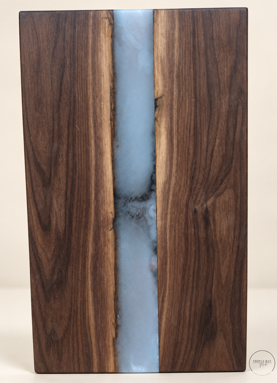 Upright view of walnut board with a pale blue-gray resin river bordered by lighter wood