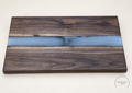 Premium walnut serving board with a pale blue-gray resin river and smoky center, angled front view