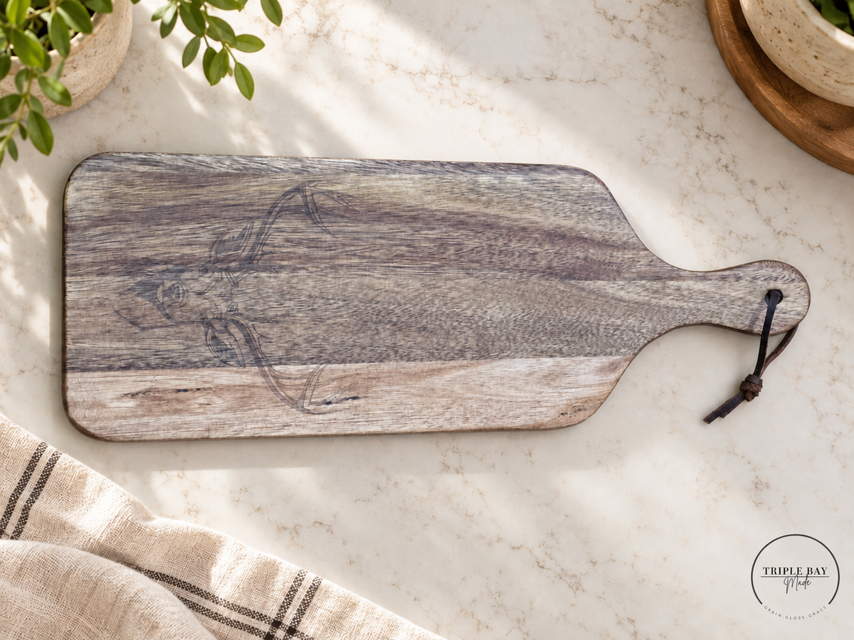 Longhorn-engraved acacia paddle board on a light stone counter beside neutral linen and greenery