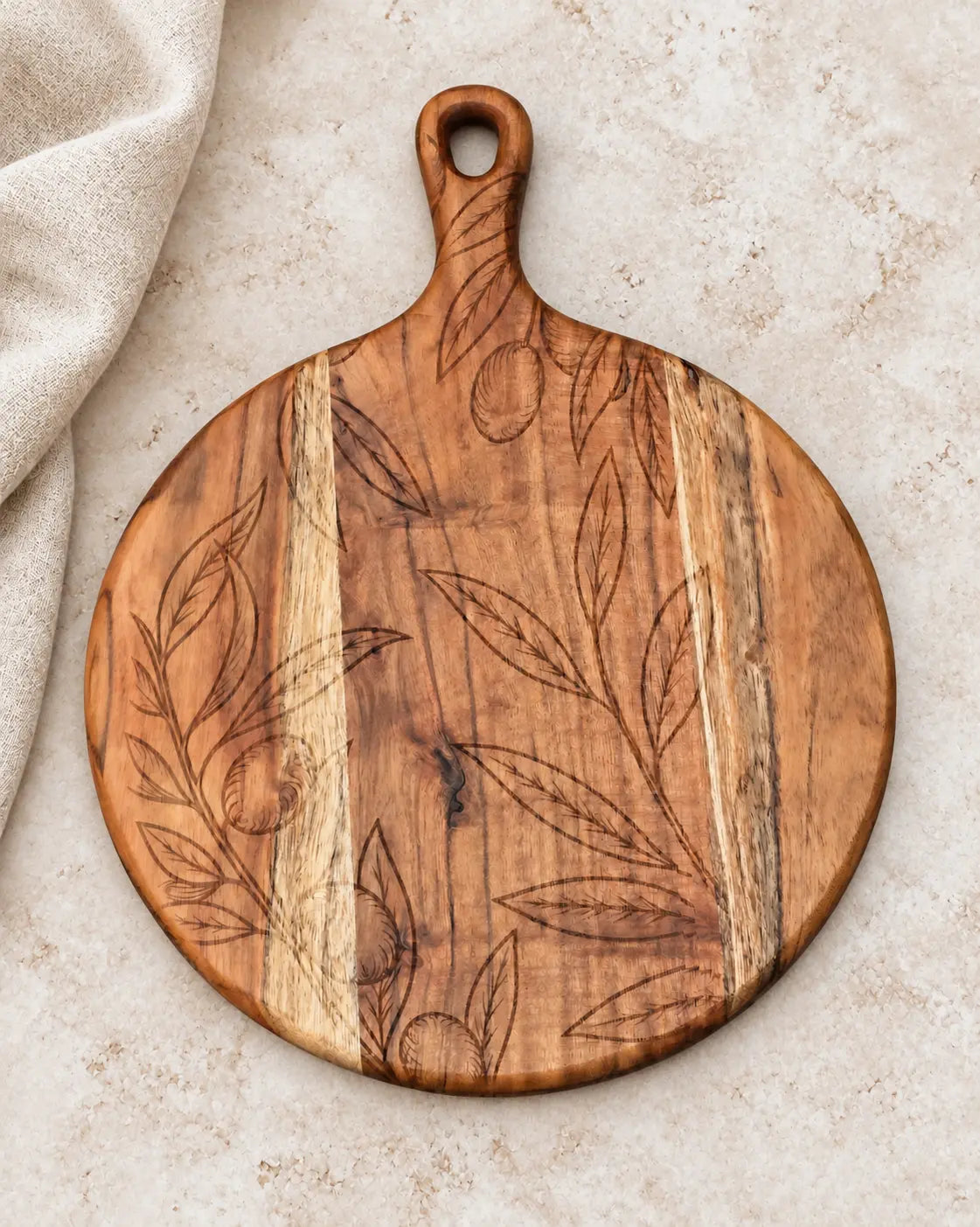 Botanical engraved acacia serving board styled on ivory stone beside neutral linen