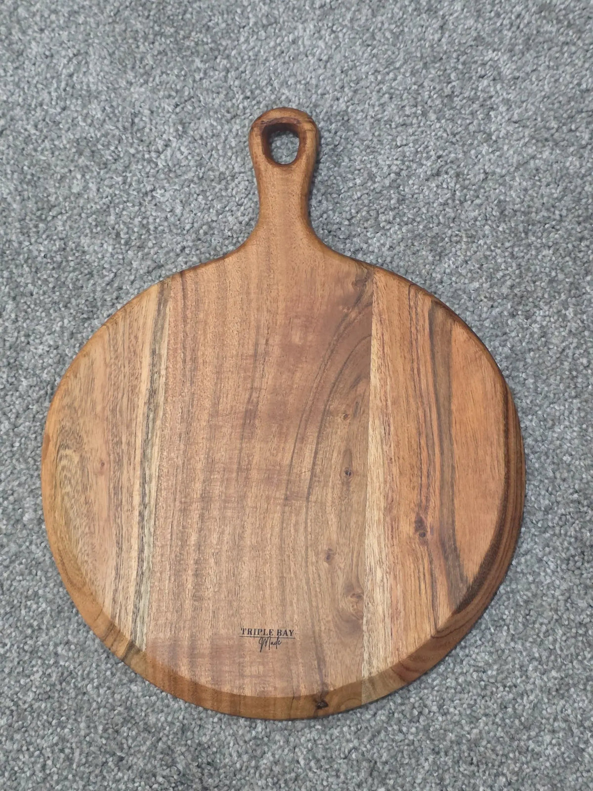 Reverse of round acacia paddle board with natural golden-brown grain and Triple Bay Made maker mark