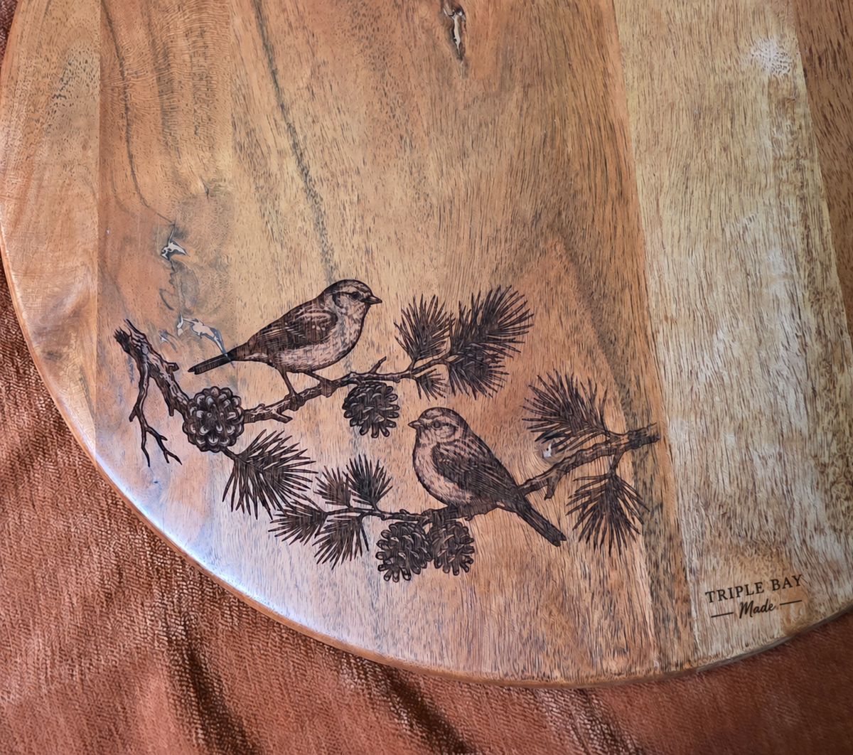 Close-up of birds, pine needles and cones engraved on Pine & Song board