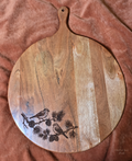Pine & Song round acacia serving board with two engraved birds and pine branches