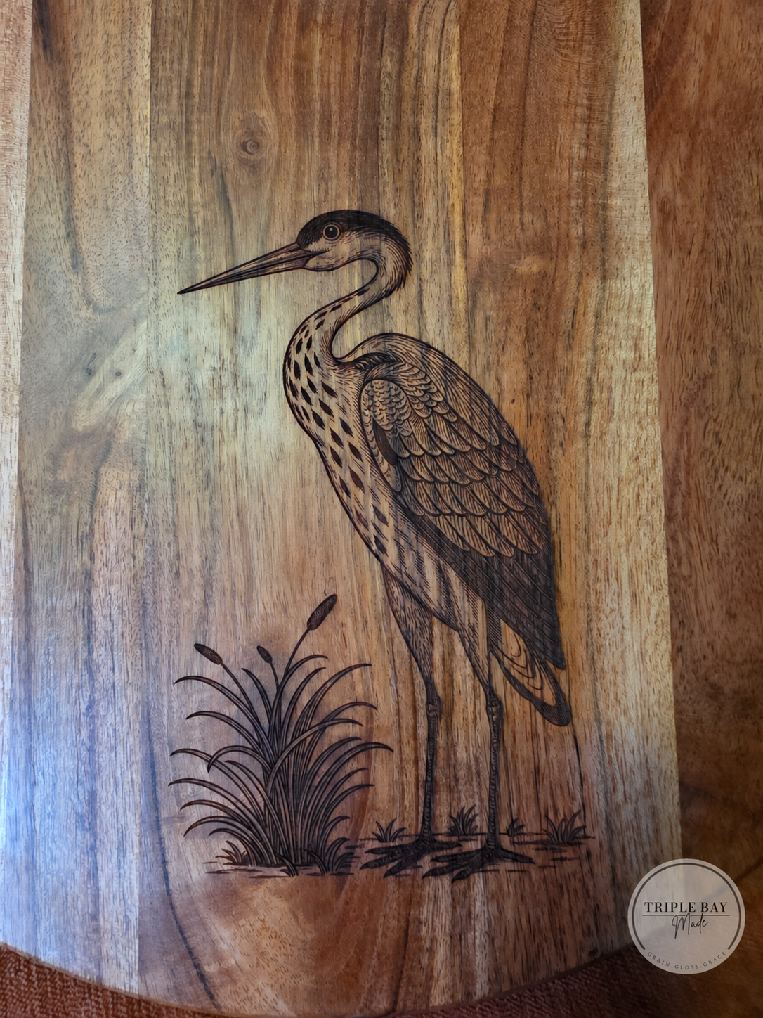 Close-up of the engraved heron's feathers and cattails against acacia wood grain