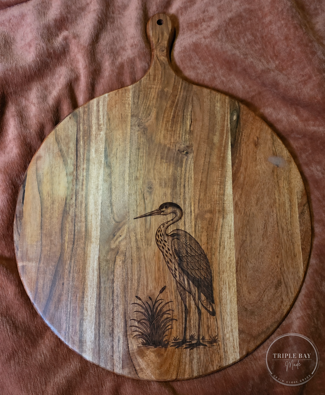 Round acacia paddle serving board with a heron and cattail engraving on the front