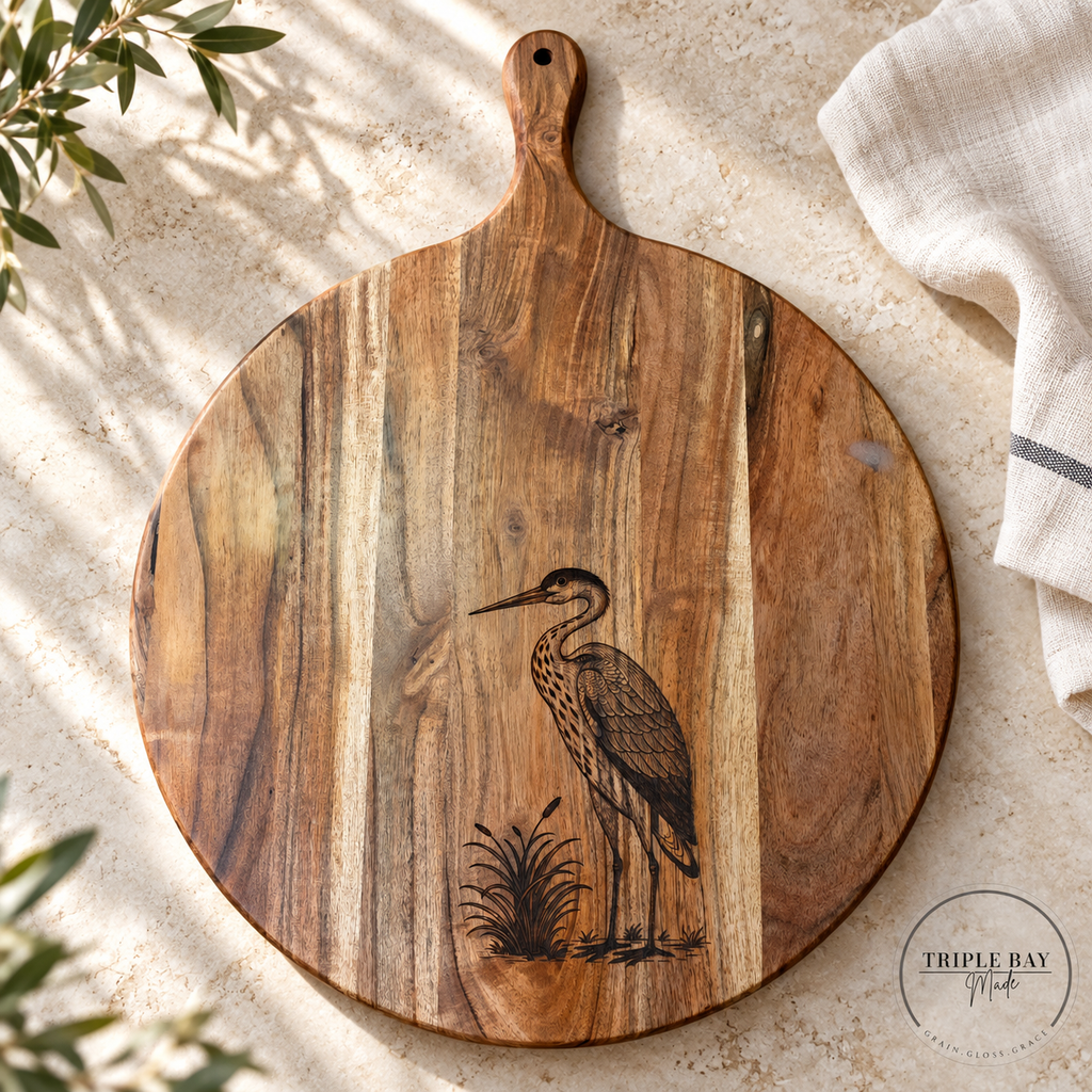 Heron engraved acacia serving board on a light stone counter beside ivory linen