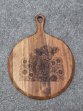 Round acacia serving board with handle, engraved with a shaggy calf surrounded by sunflowers