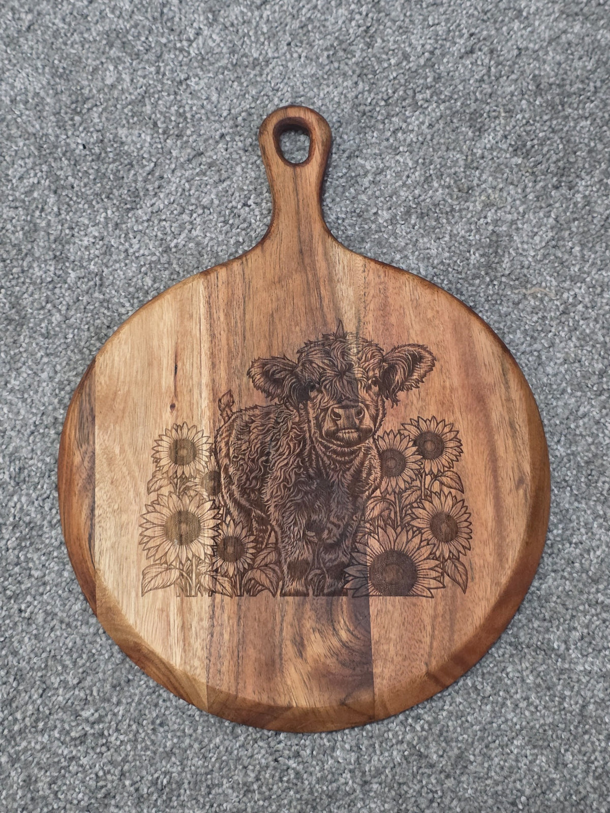 Round acacia serving board with handle, engraved with a shaggy calf surrounded by sunflowers