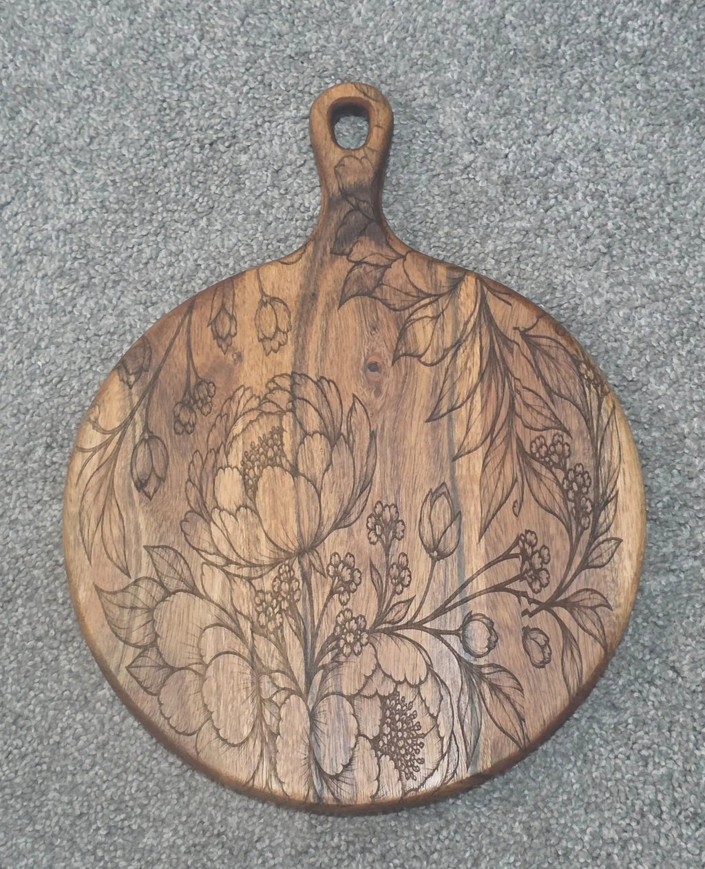 Round acacia paddle serving board with engraved flowers, buds and sweeping leaves
