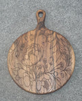 Round acacia paddle serving board with engraved flowers, buds and sweeping leaves