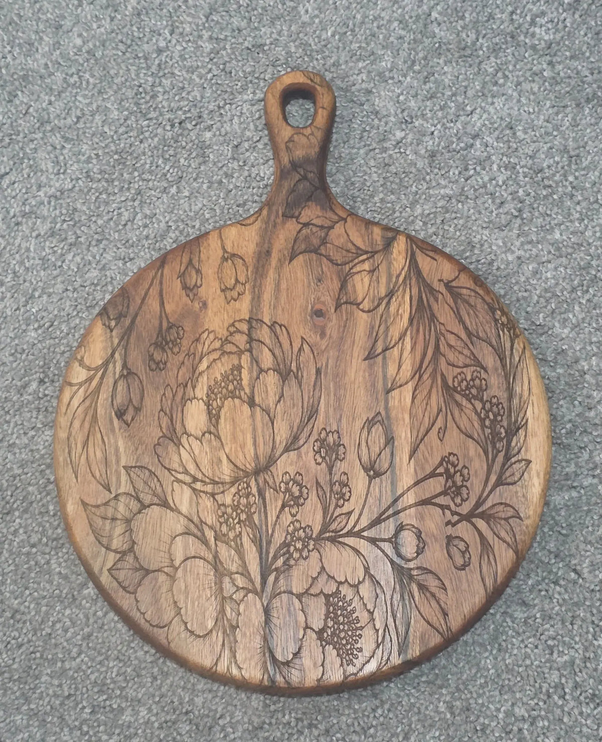 Round acacia paddle serving board with engraved flowers, buds and sweeping leaves
