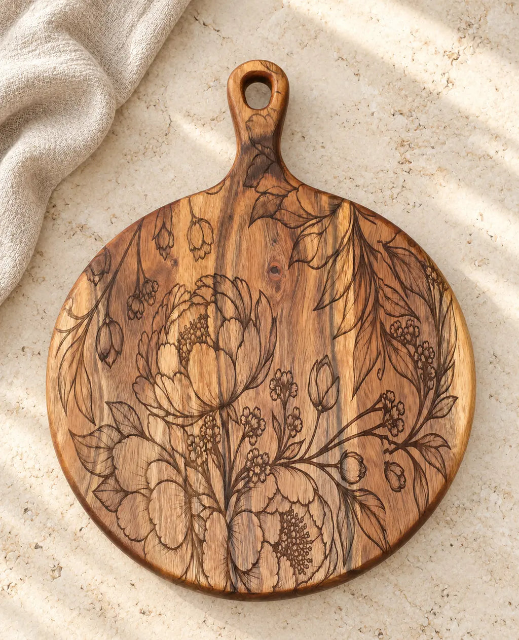 Floral engraved round acacia serving board on ivory stone beside folded neutral linen