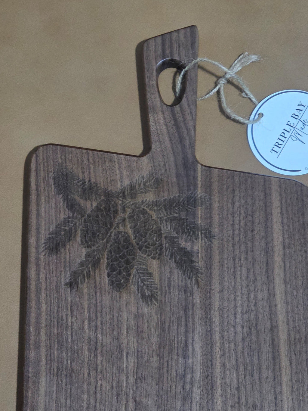 Detail of pinecone and evergreen engraving on walnut-finished acacia board